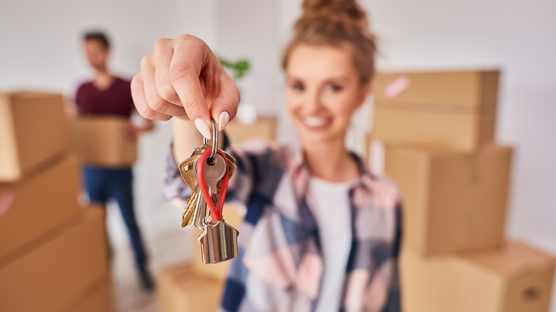 A couple in their moving day. The lady handling the key of the house while her significant other is carrying box of stuff behind her.