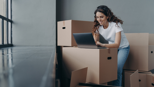 Female with boxes works at laptop, orders moving company