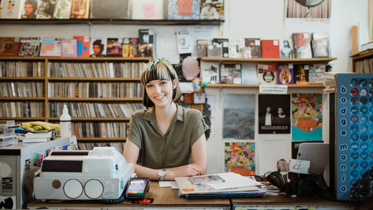 Female owner standing behind the counter in a record store smiling at the camera