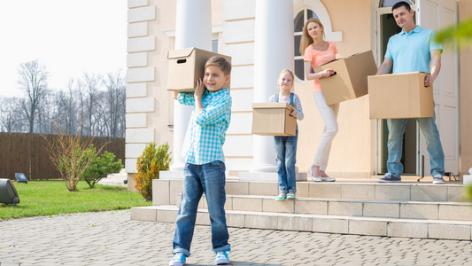 This small family moving out to their house, little boy infront carrying box of stuff followed  by her little sister, Mom and Dad