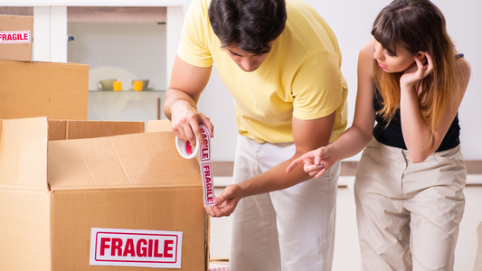 Couple packing stuff and putting a fragile label to boxes with breakable stuff inside.