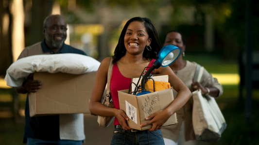 Family moving daughter into her new dorm for the first time. The young college girl is smiling and excited. The mom and dad are walking close behind her, and following with happiness.