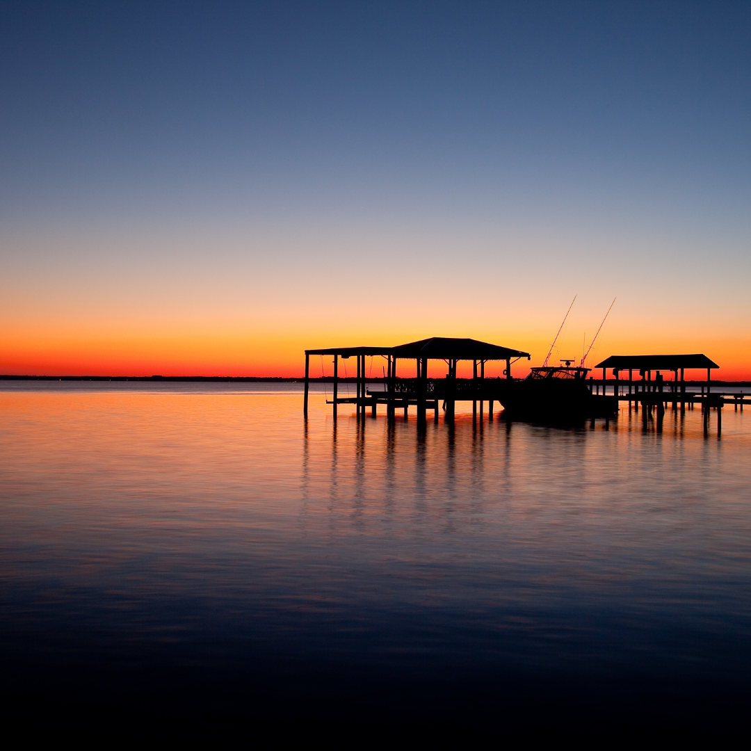 A picturesque sunset over a boat dock, with a few boats peacefully anchored in the water.