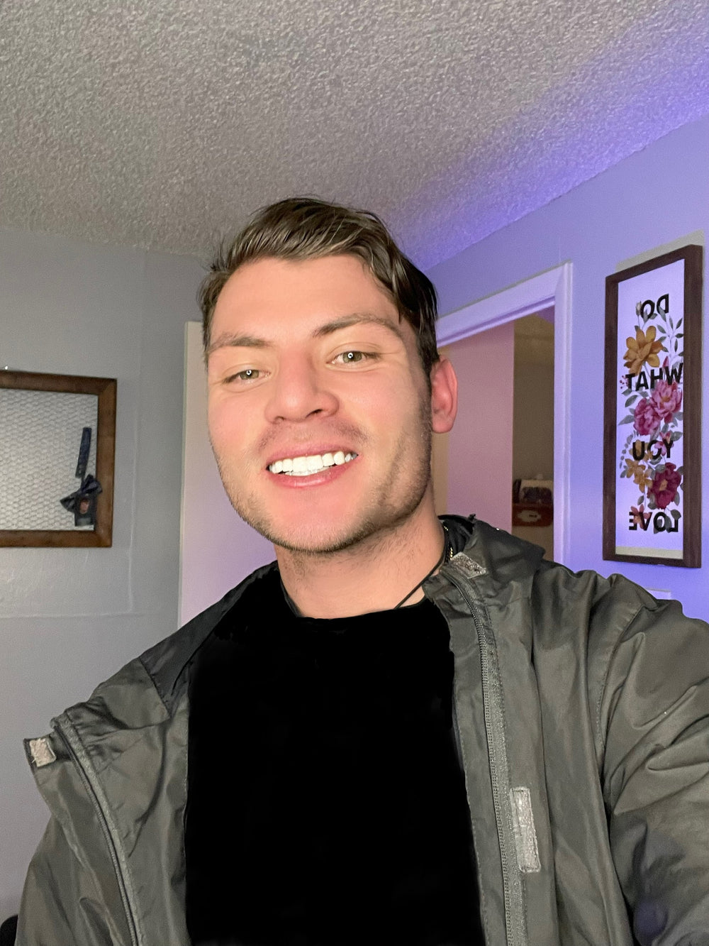 alt="A man wearing a black shirt and jacket smiles warmly"