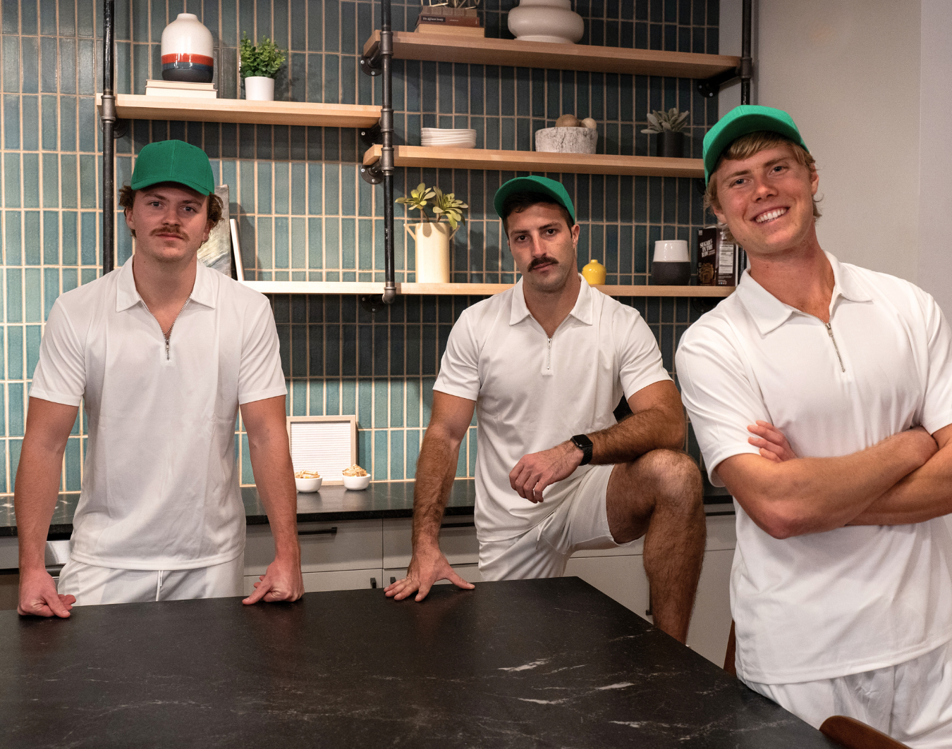 alt="3 men wearing white polo and green cap"