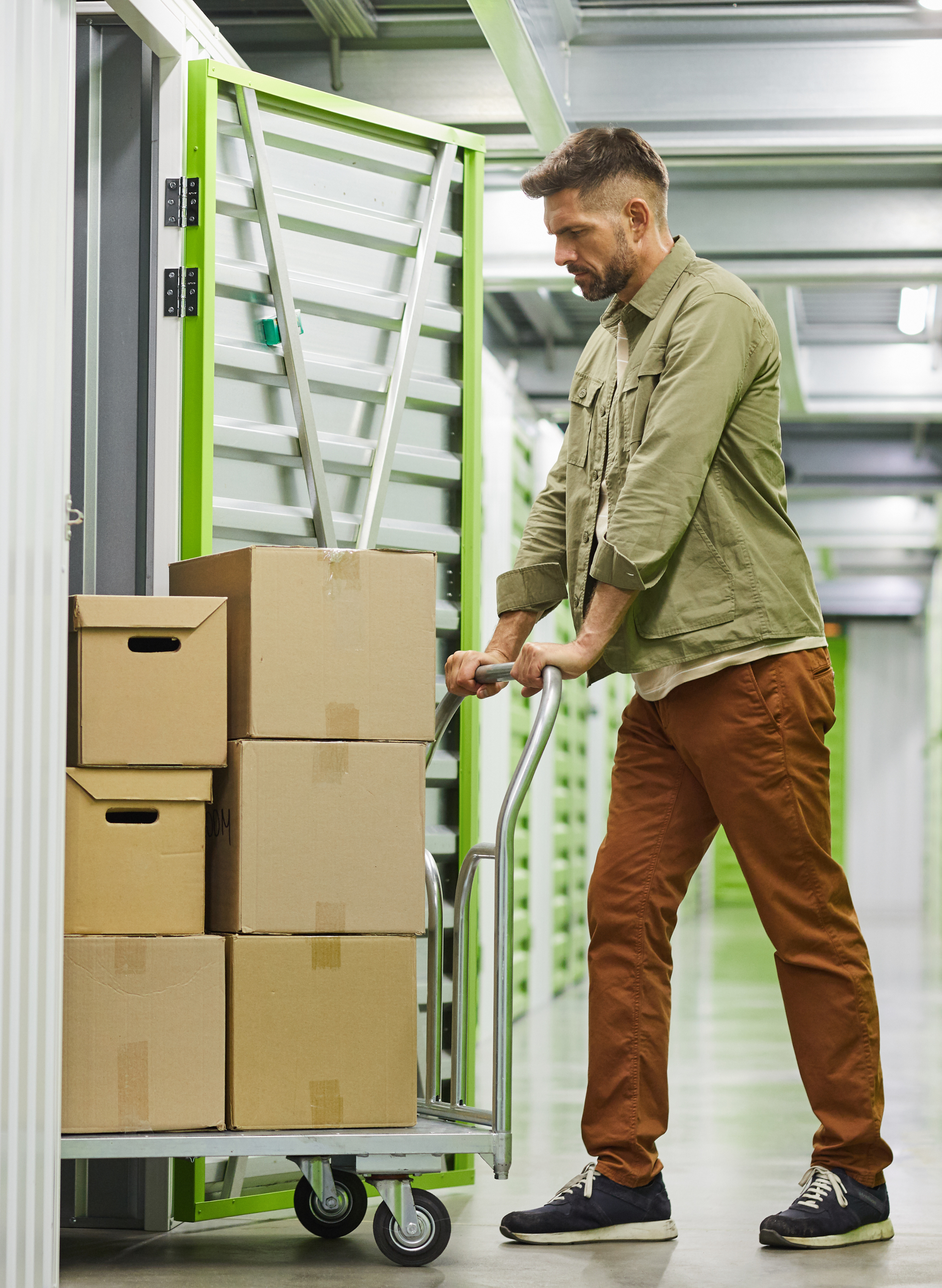 alt="a man pushing a cart of boxes into a green and grey storage unit"