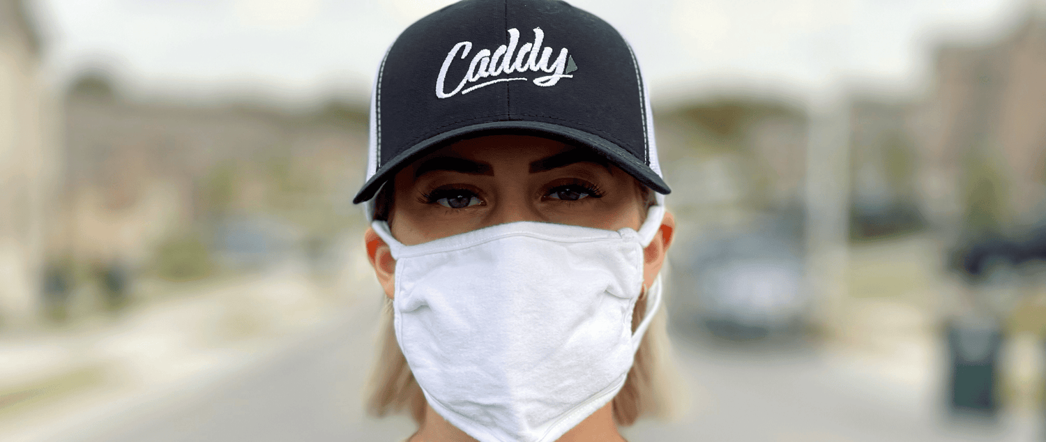 <img src=“mover with face mask.png” alt=“young woman mover wearing Caddy moving hat looking at camera wearing white face mask”>