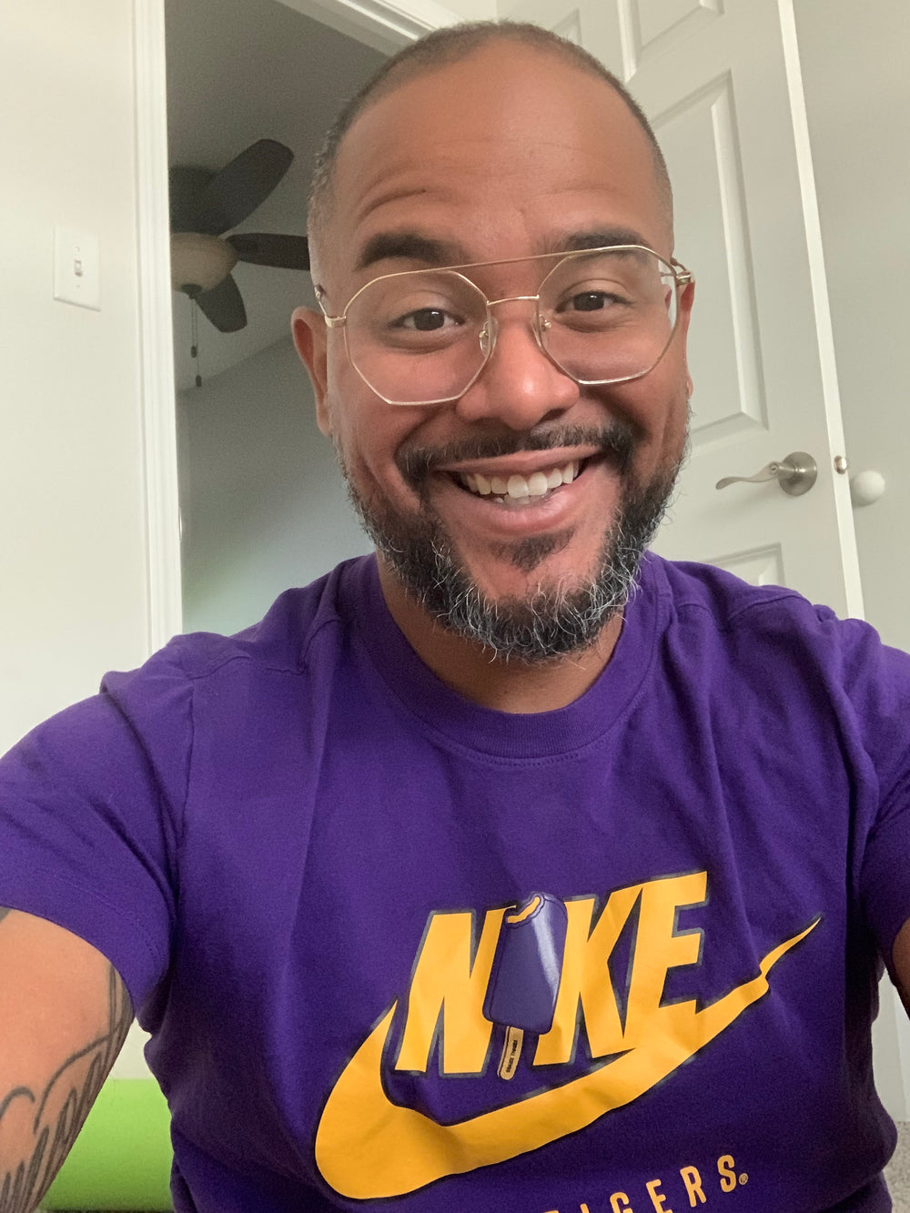 alt="A cheerful man in a purple shirt and glasses, smiling warmly at the camera"